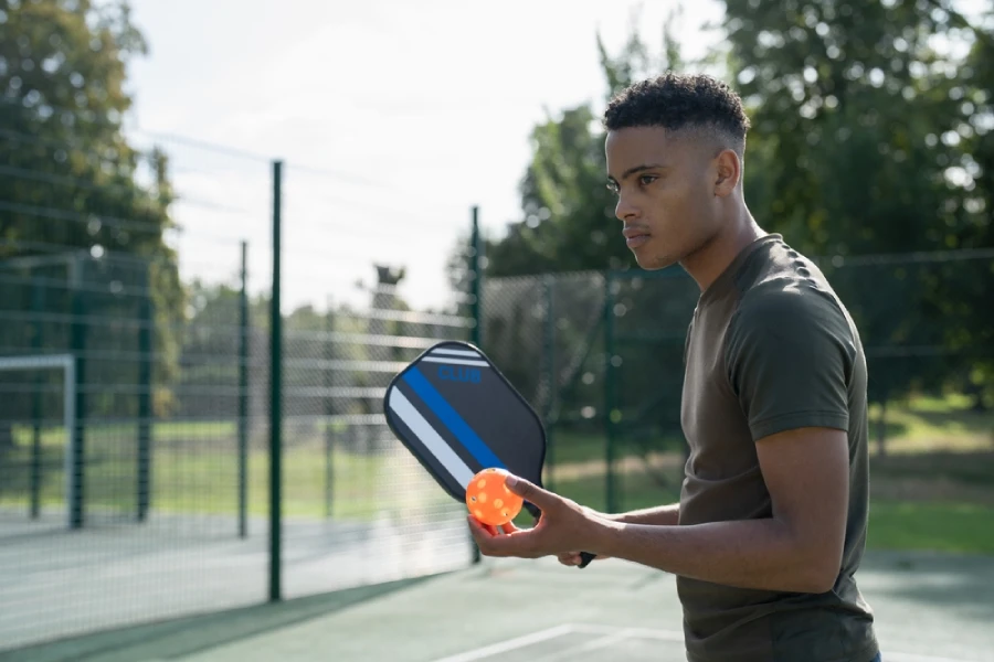 all-round player holding a pickleball paddle and orange ball in outdoor court