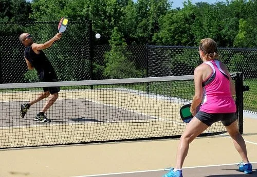 Two players in a pickleball game, with one performing a volley close to the net while the opponent prepares to return the shot.